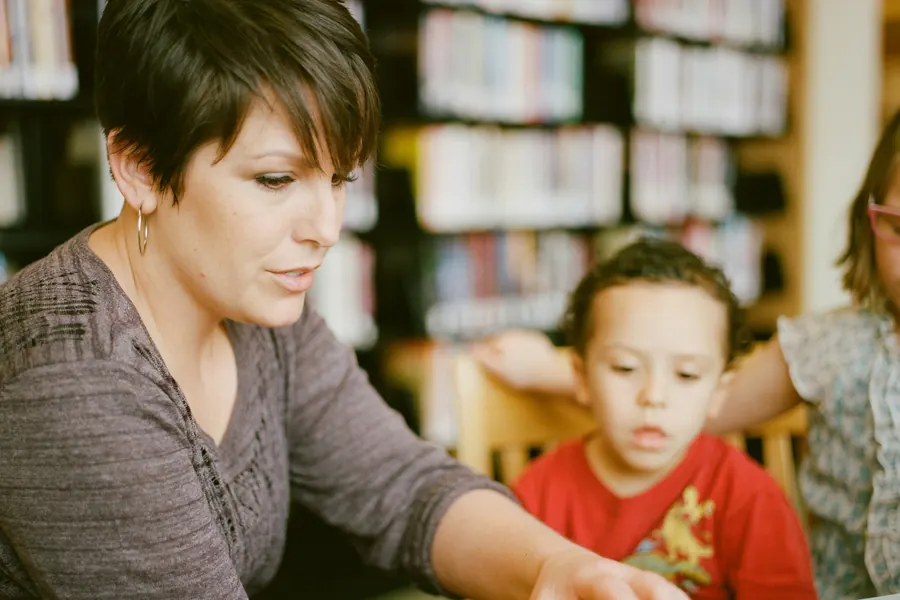 A woman reading with a young boy at a library table