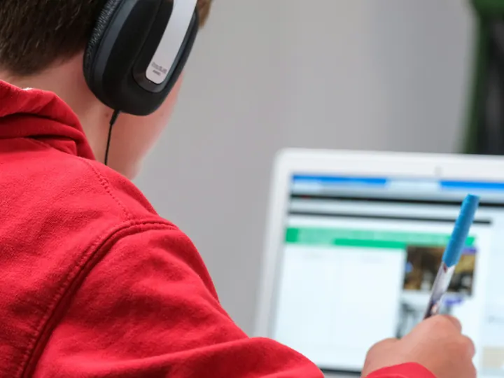 A student wearing headphones takes notes during an online lesson